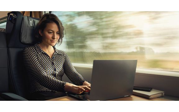 Frau sitzt im Zug und ist auf einen Laptop fokussiert.