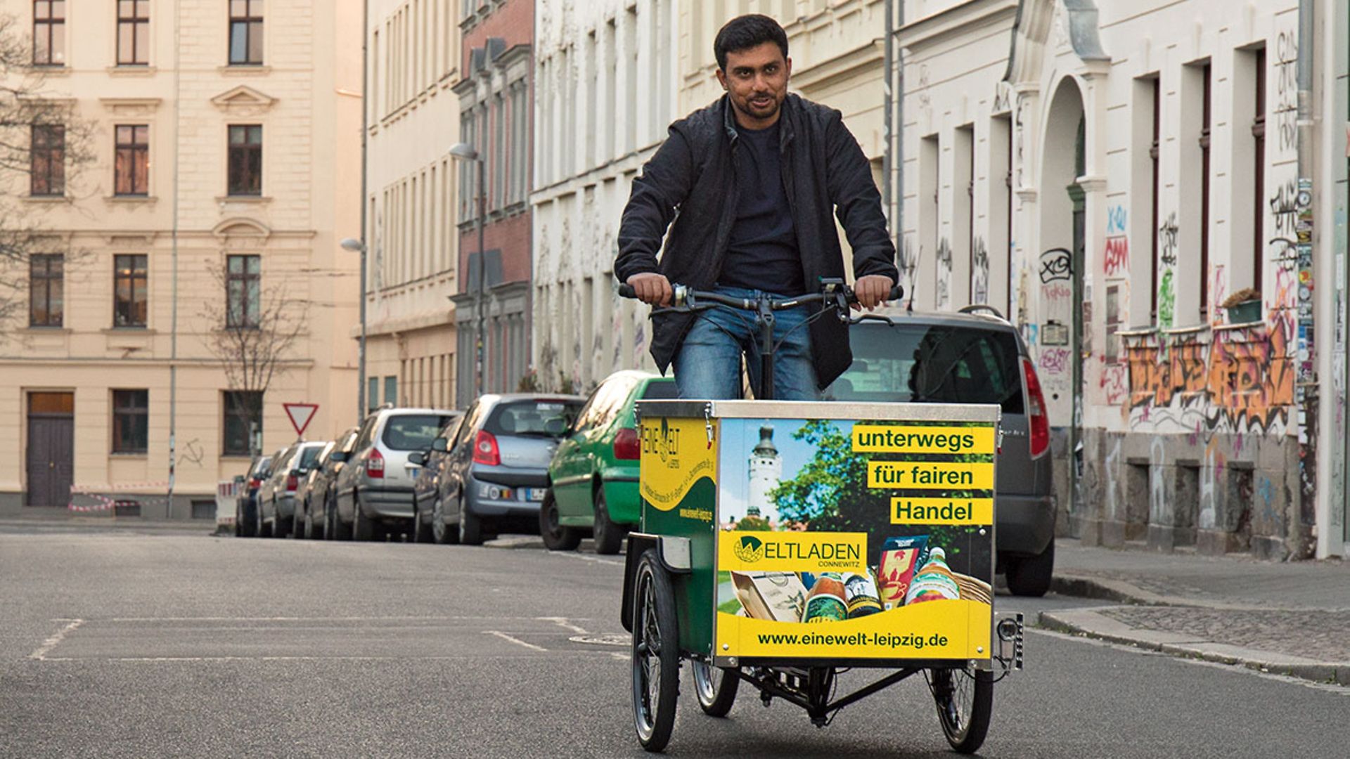 Mann fährt mit Lastenfahrrad des Eine Welt Laden vor Häuserfront