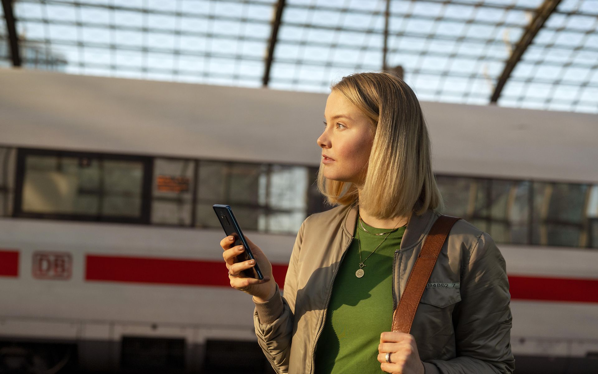 Frau mit Handy in der Hand, im Hintergrund ein ICE
